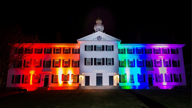 A photo of Dartmouth Hall at night lit up with rainbow colored lights.