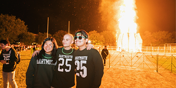 A group of three 25s standing in front of the Dartmouth homecoming bonfire