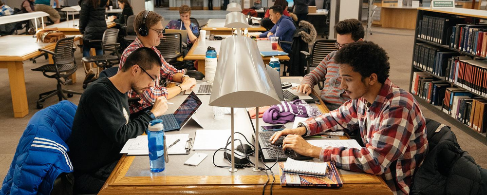 Four students working on laptops in the library.