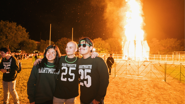 Three students posing for a photo on bonfire night. Two of them are wearing Dartmouth 25 shirts.