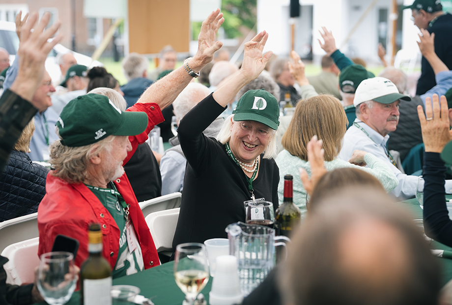A pair of reunions attendees smile and raise their hand at an event