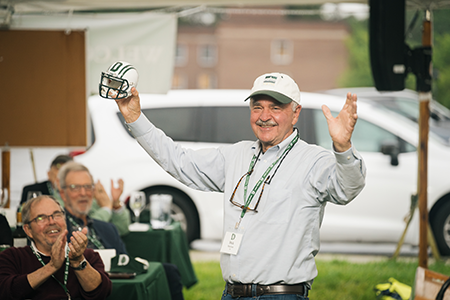 A man holding a football helmet with his hands stretched out and smiling