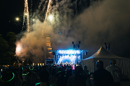 fireworks illuminate the night sky behind a green-lit Baker Bell Tower