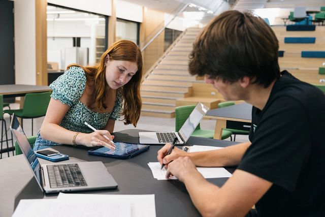 Two students seated at a table working on assignments