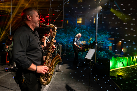 Saxophonist in foreground with lights streaming around at night