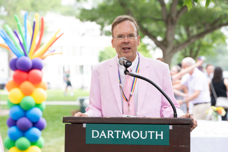 A person speaking behind a podium that says Dartmouth in front of a tower of rainbow balloons.