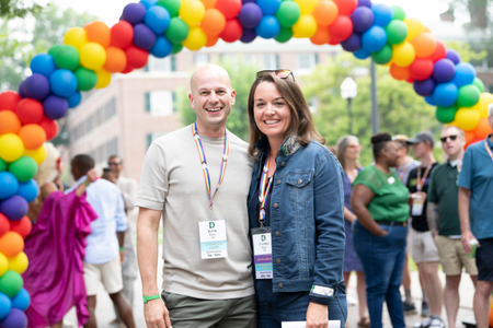 Two people posing below a balloon arch. 