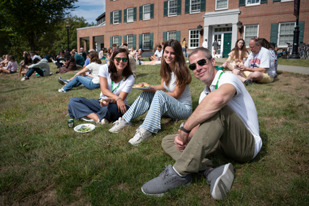 A family sitting on the lawn in front of a residence hall.