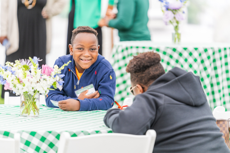 Two tweens in attendance at seated at a table with a green and white checked table cloth. 
