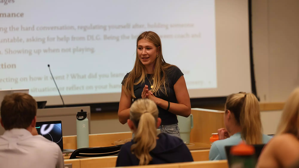 A female student-athlete speaking in front of a classroom group