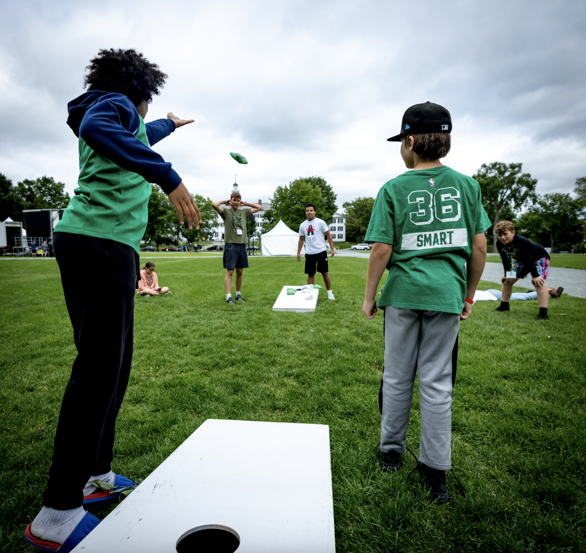 A woman and child dressed in Dartmouth gear playing cornhole on the green.