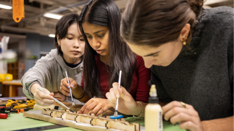 Three students working on a model sitting on a table top.