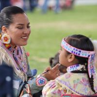 A woman brushes paint on her young daughter's chin at the Dartmouth powwow