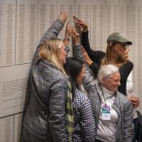 Four Dartmouth alumnae pointing at their names on the donor wall in Dartmouth Hall